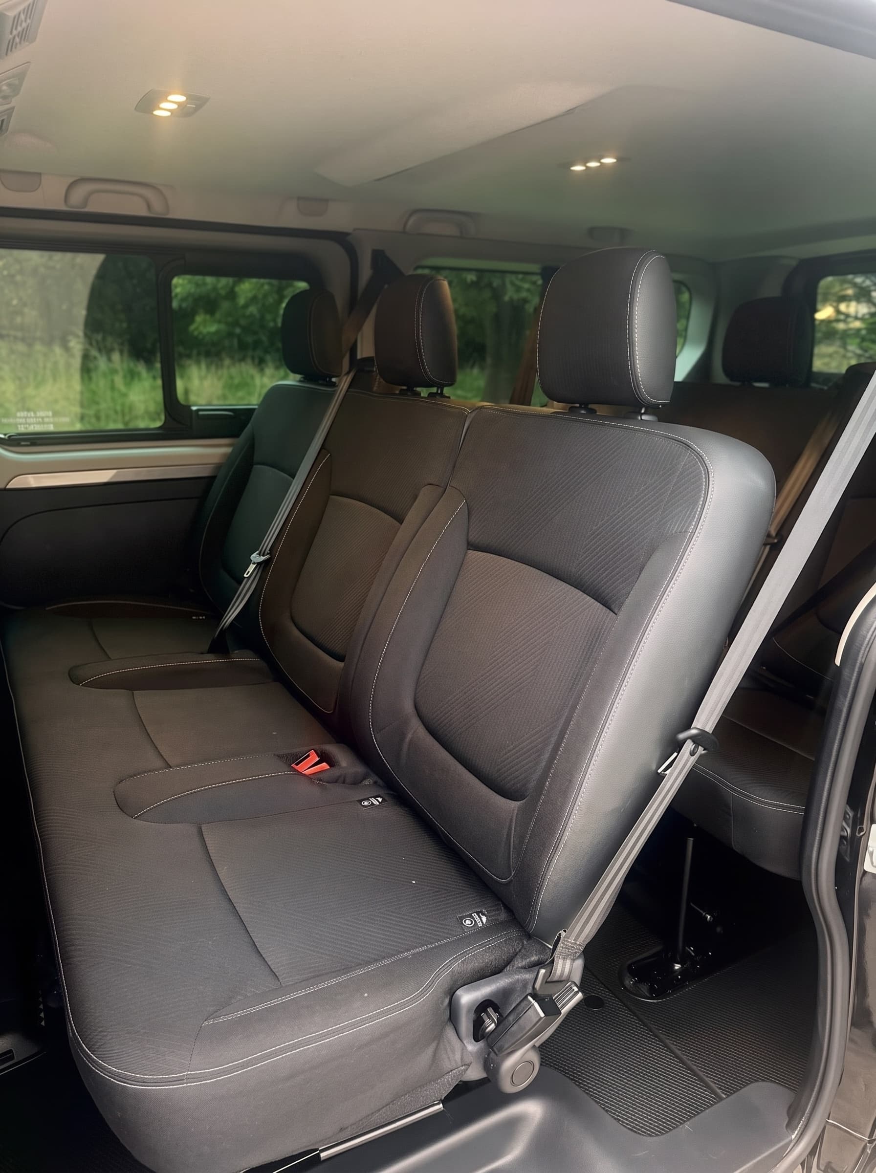 A rear bench seat in the Trafic seen through the open side door, with fabric seats, seatbelts fitted and a further row of seats behind.
